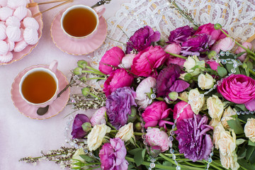 on a pink background a bouquet of ranunculus, two cups of tea and meringue