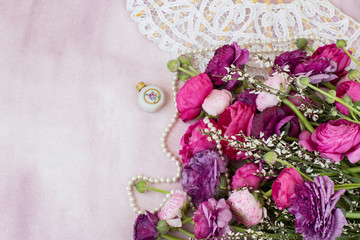 on a pink background a bouquet of ranunculuses, a bottle of perfume, pearl beads and a white fan