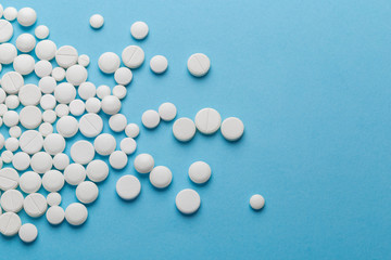 scattered white pills on a blue table. Layout for special offers such as advertising or other ideas. The concept of medicine, pharmacy and healthcare. Space for copy. flat lay for text or logo.