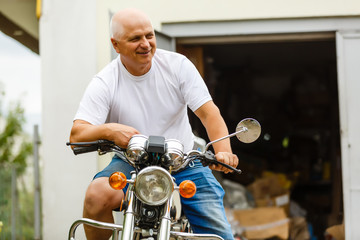 An elderly man sitting on a motorcycle.