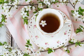 cup of tea, napkin and branches of blossoming cherry closeup on white wooden background