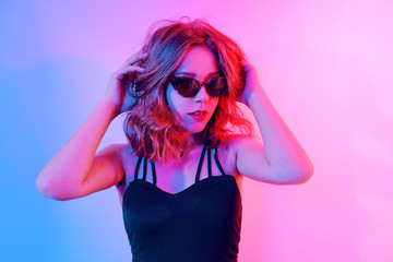 Beautiful girl in neon. Fashion photo of a short-haired girl, dancing, sun glasses. Girl in red and blue light posing.