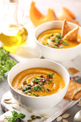Concept of Russian cuisine. Pumpkin cream soup with cookies on a light background. Pumpkins, olive oil, spices, spoon, pumpkin seeds, herbs. Background image, copy space