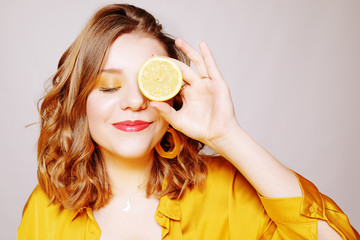Portrait of a girl with a lemon. A girl in a bright yellow dress, with yellow earrings, holds a lemon. Sincere smile. covering eye with limon and blowing kiss