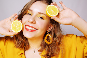 Clouse up of a girl with a lemon. A girl in a bright yellow dress, with yellow earrings, holds a lemon. Sincere smile. covering eye with limon.