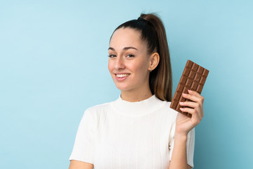 Young brunette woman over isolated blue background taking a chocolate tablet and happy