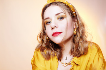 Beautiful young short-haired girl looking at the camera smiling. Girl with professional yellow make-up, bandage on her head, beautiful large earrings on a yellow background.