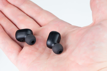 a pair of black wireless earbuds laying on caucasian palm - close-up with selective focus