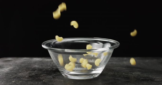 Raw Pasta falling in bowl isolated on black background. 4k resolution, slow motion
