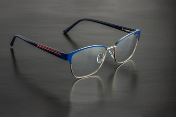 The female golden and blue medical eyeglasses lying on a black surface