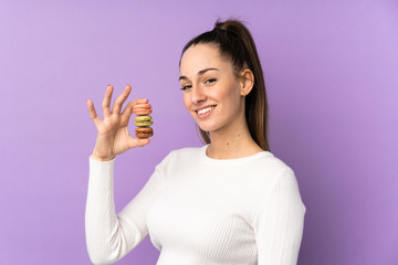 Young brunette woman over isolated purple background holding colorful French macarons and smiling a lot