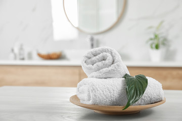 Rolled fresh towels and green leaf on white table in bathroom. Space for text