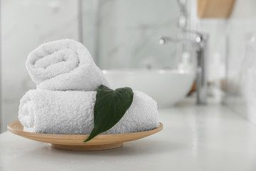 Rolled fresh towels and green leaf on white table in bathroom
