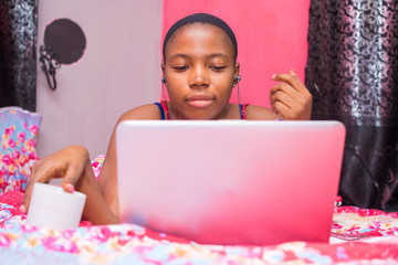 pretty african lady at home alone in her bedroom, watching a movie on her laptop pc