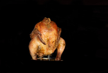 Chicken carcass in the oven. A whole cooked appetizing chicken with garlic and spices. Around black background
