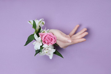 Obraz na płótnie Canvas Beauty Hand with flowers in a hole in a purple paper background. Nature hand Cosmetics, natural flower extract, moisturizing and softening the skin