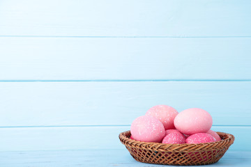 Pink easter eggs in basket on blue wooden background