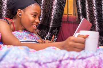 pretty african lady at home alone in her bedroom, watching a movie on her laptop pc