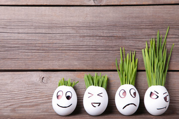 Cute handmade eggs with hair of green grass with copy space. Easter concept on grey background