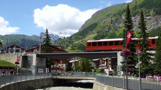 Red train in Zermatt, luxury alpine ski resort town. Scenic railway across Swiss Alps to Matterhorn mountain. Switzerland summer tourism destination, 4k.