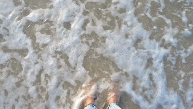 top view of bare woman feets standing on a sandy beach and washed by the sea waves