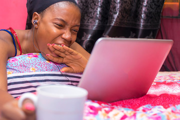 pretty african lady at home alone in her bedroom, watching a movie on her laptop pc, yawning