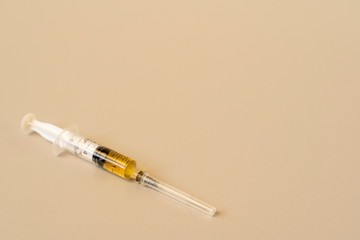 Syringe with yellow liquid on a beige background.
