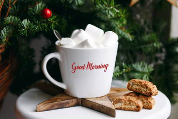 Coffee in a white cup with marshmallows. Morning festive coffee with traditional Italian cantuccini almond cookies. A cup of coffee on a background of green fir branches on a white stand.