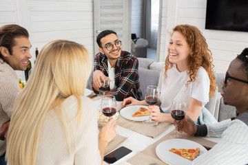 Horizontal high angle shot of young men and women chatting while having meal in modern apartment