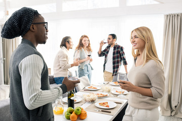 Group of young people spending weekend together in modern apartment drinking wine and chatting