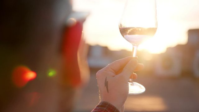 Man in sunglasses looks at glass of wine. Glass of white or rose wine in sunset light. Enjoy sophisticated sommelier experience during wine tasting. Cinematic lifestyle in rooftop bar