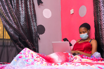 lady in her bedroom wearing a face mask using her laptop pc and smartphone