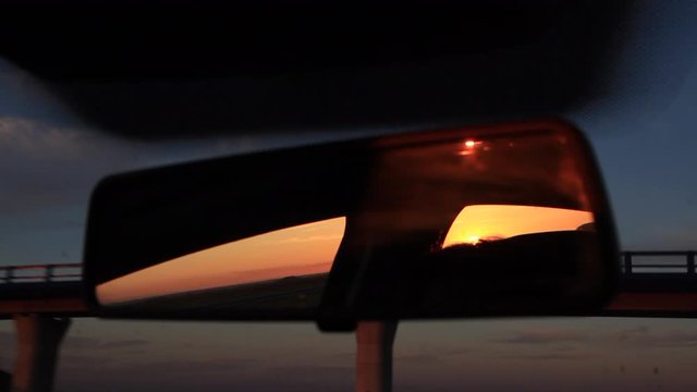 Interior rearview of moving car reflecting a sunset at sunset. Crossing a bridge or overpass