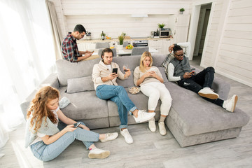 Horizontal shot of modern young people watching something on their smartphones instead of interacting with each other