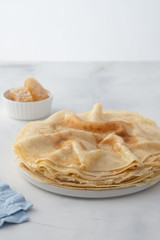 Crepes, thin pancakes with honey on a white plate. Marble background. Close up.