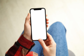 Woman in shirt and jeans holding phone with empty screen