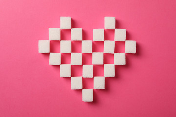 Heart made of sugar cubes on pink background, top view