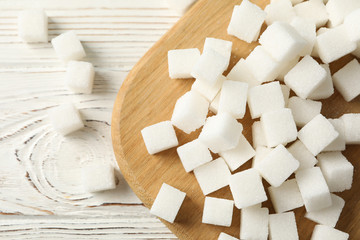 Board with sugar cubes on wooden background, top view