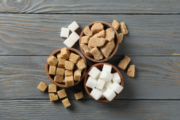 Bowls with different sugar on wooden background, top view