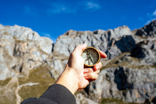 Man using a compass to orient himself by the mountain on a sunny day.