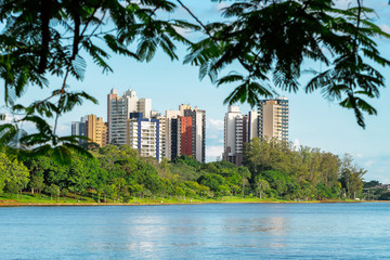 Fototapeta na wymiar View of a city lake through the tree leaves. Lake surrounded by nature and few buildings on the background. Photo of the Igapo lake, Londrina PR Brazil.