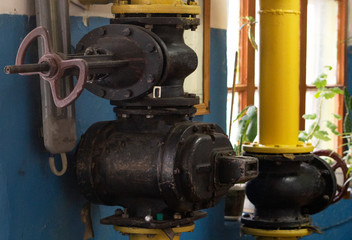 Fototapeta na wymiar In the foreground is a black gate valve with a diameter of 150 millimeters above the old gas meter in the boiler room. In the background is another valve.