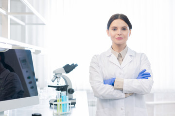 Confident Caucasian woman wearing white lab coat and gloves standing with arms crossed looking at camera