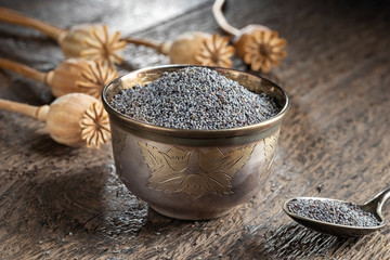 Poppy seeds in a cup with poppy pods in the background