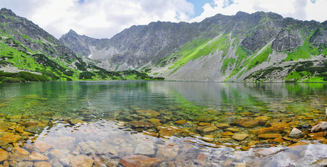 Fototapeta na wymiar Glittering mountain lake. Lower Temnosmrečianske Lake. The lake surrounded by majestic and high cliffs. High Tatras national park, Slovakia. 
