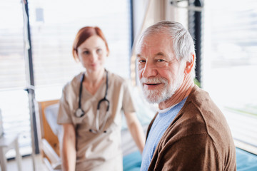 Senior patient and doctor sitting on bed in hospital, looking at camera.