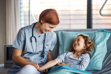 Friendly female doctor examining small girl in bed in hospital.