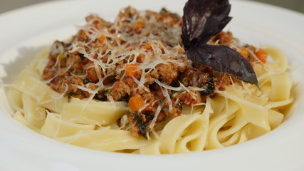 Close-up of rotating white plate with pasta bolognese with parmesan cheese and basil leaves on top. Italian food concept