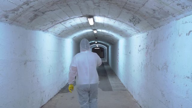 man in bio hazard protective suit with respirator mask and gloves walks in a uninhabited corridor with a respirator in his hand and treats infection, scared and runs away.  Novel coronavirus - 2019-nC
