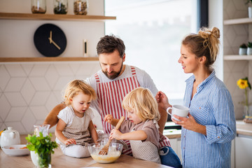 Young family with two small children indoors in kitchen, cooking.